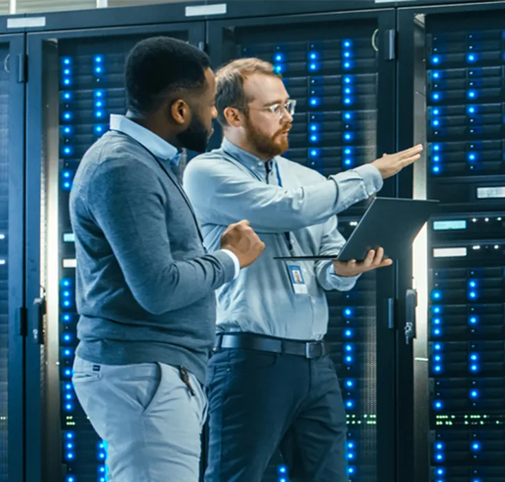 Two men using laptop in front of computer servers